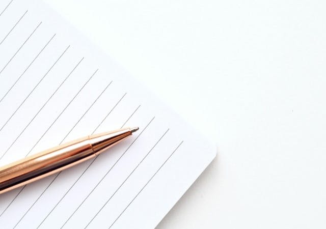 A lined notebook and a copper pen located on top of it.