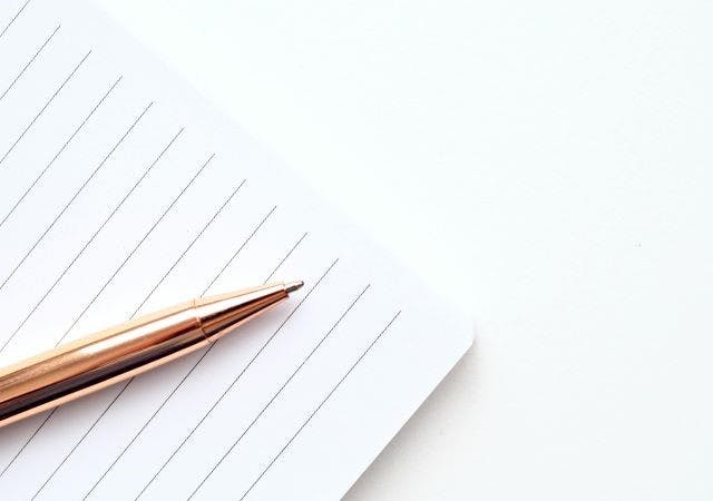 A lined notebook and a copper pen located on top of it.